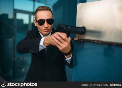 Bodyguard in suit and sunglasses with a gun in his hands. Security guard is a risky profession, professional guarding, politicians and business persons protection from the danger of life. Bodyguard in suit and sunglasses with gun in hands