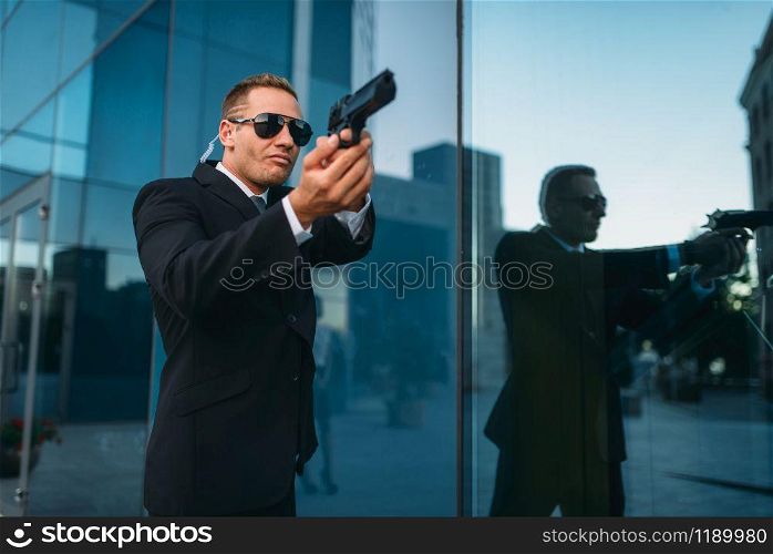 Bodyguard in suit and sunglasses with security earpiece and gun in his hands. Guarding is a risky profession, politicians and business persons protection from the danger of life. Bodyguard with security earpiece and gun in hands
