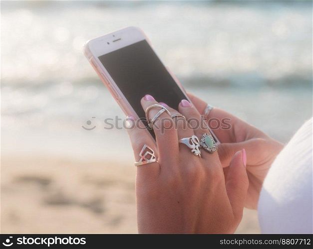Boho gypsy woman using smartphone on beach near sea. Lot of silver rings. High quality photo. Boho gypsy woman using smartphone on beach near sea. Lot of silver rings.
