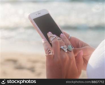 Boho gypsy woman using smartphone on beach near sea. Lot of silver rings. High quality photo. Boho gypsy woman using smartphone on beach near sea. Lot of silver rings.