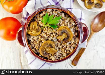 Boiled buckwheat with champignon in a brown pottery bowl on a kitchen towel, tomatoes in the background light from the top of the board