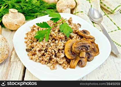 Boiled buckwheat with champignons in white plate, dill, parsley and kitchen towel on a background of light board
