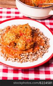 Boiled buckwheat with meatballs under tomato sauce on the plate. Buckwheat with meatballs