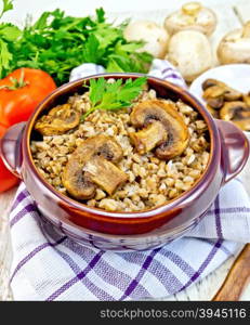 Boiled buckwheat with mushrooms in a brown pottery bowl on a kitchen towel, parsley on a light background boards