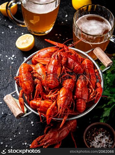 Boiled crayfish in a colander and a glass of beer. On a black background. High quality photo. Boiled crayfish in a colander and a glass of beer.
