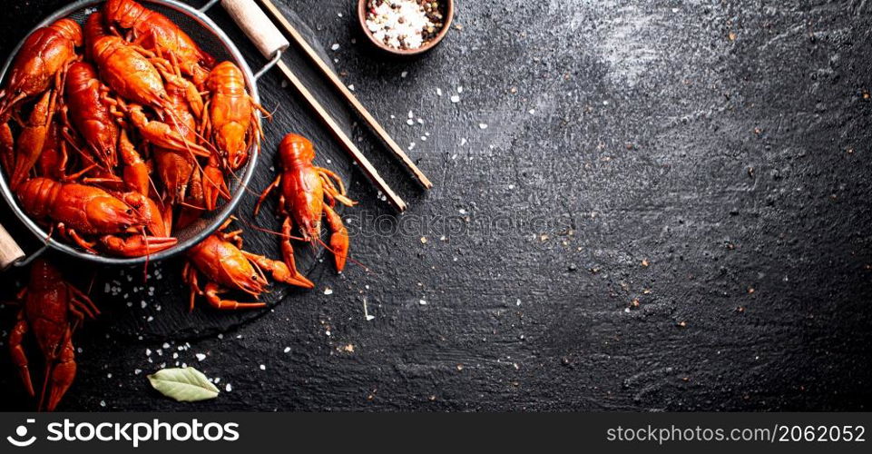 Boiled crayfish in a colander on a stone board. On a black background. High quality photo. Boiled crayfish in a colander on a stone board.