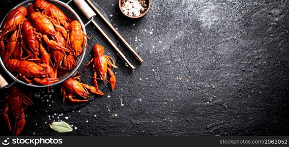 Boiled crayfish in a colander on a stone board. On a black background. High quality photo. Boiled crayfish in a colander on a stone board.