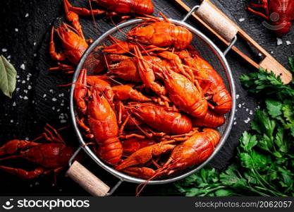 Boiled crayfish in a colander on a stone board. On a black background. High quality photo. Boiled crayfish in a colander on a stone board.