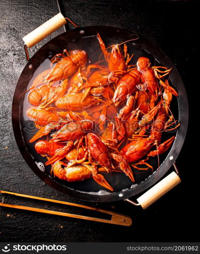 Boiled crayfish in a pot of water. On a black background. Top view. High quality photo. Boiled crayfish in a pot of water.