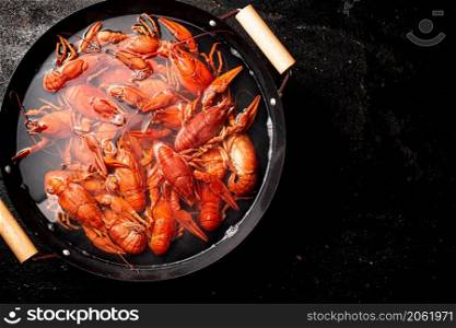 Boiled crayfish in a pot of water. On a black background. Top view. High quality photo. Boiled crayfish in a pot of water.