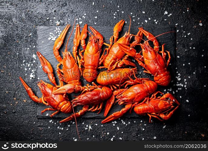 Boiled crayfish on a stone board with salt. On a black background. High quality photo. Boiled crayfish on a stone board with salt.