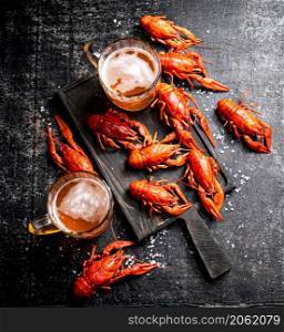 Boiled crayfish with beer on a cutting board. On a black background. High quality photo. Boiled crayfish with beer on a cutting board.