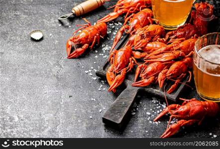 Boiled crayfish with beer on a cutting board. On a black background. High quality photo. Boiled crayfish with beer on a cutting board.