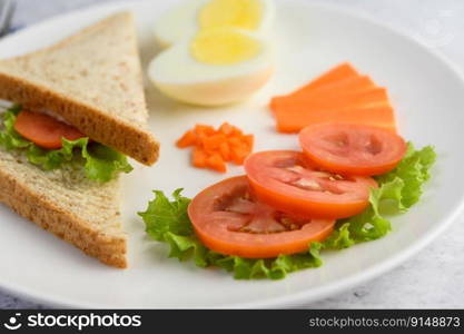 Boiled eggs, bread, carrots, and tomatoes on a white plate with a knife and fork. Selective focus.