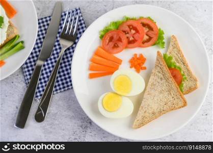 Boiled eggs, bread, carrots, and tomatoes on a white plate with a knife and fork. Selective focus.