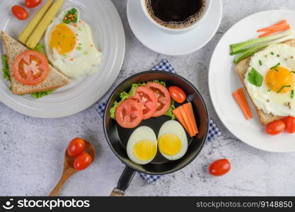 Boiled eggs, carrots, and tomatoes on a pan with tomato on a wooden spoon and coffee cup.