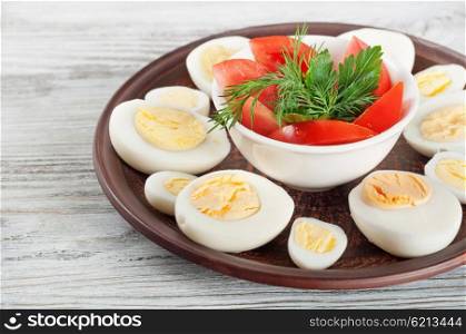 Boiled hen eggs and red tomato in a clay dish on a wooden background
