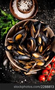 Boiled mussels in a bowl on the table. On a black background. High quality photo. Boiled mussels in a bowl on the table.