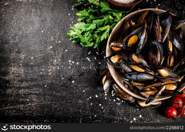 Boiled mussels in a bowl with parsley. On a black background. High quality photo. Boiled mussels in a bowl with parsley.