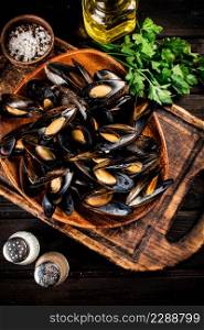 Boiled mussels in a plate on a cutting board with parsley and spices. On a wooden background. High quality photo. Boiled mussels in a plate on a cutting board with parsley and spices.