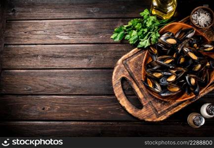 Boiled mussels in a plate on a cutting board with parsley and spices. On a wooden background. High quality photo. Boiled mussels in a plate on a cutting board with parsley and spices.