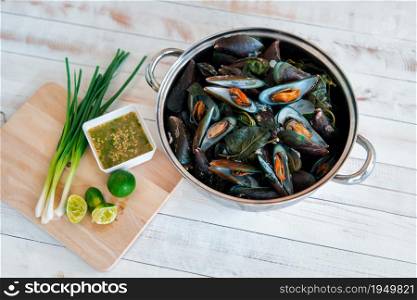 Boiled or steamed mussels premium grade is seafood display with seafood sauce (chilli, garlic, lime) have sour and savory on white table for sale at Thai street food market or restaurant in Bangkok. Steamed mussels and seafood sauce on white table