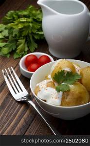 Boiled potatoes with cherry tomatoes, parsley and sour cream on wooden table