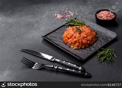 Boiled rice with peppers, spices, herbs and tomato sauce on a black slate plate on a grey concrete background. Boiled rice with peppers, spices, herbs and tomato sauce on a black slate plate
