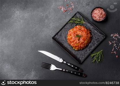 Boiled rice with peppers, spices, herbs and tomato sauce on a black slate plate on a grey concrete background. Boiled rice with peppers, spices, herbs and tomato sauce on a black slate plate
