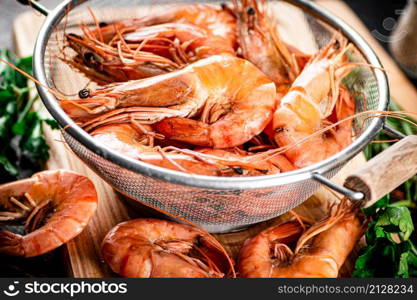Boiled shrimp in a colander on a cutting board with parsley. Against a dark background. High quality photo. Boiled shrimp in a colander on a cutting board with parsley.