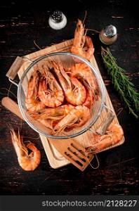 Boiled shrimp in a colander with a sprig of rosemary. Against a dark background. High quality photo. Boiled shrimp in a colander with a sprig of rosemary.