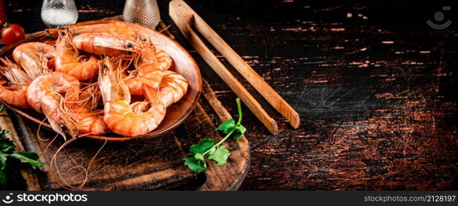 Boiled shrimp in a plate on a cutting board with spices. On a rustic dark background. High quality photo. Boiled shrimp in a plate on a cutting board with spices.