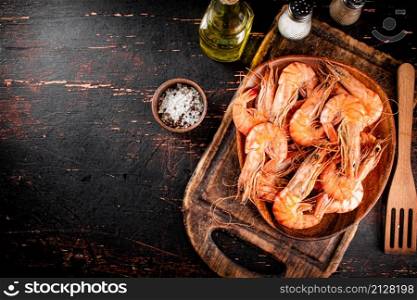 Boiled shrimp in a plate on a cutting board with spices. On a rustic dark background. High quality photo. Boiled shrimp in a plate on a cutting board with spices.