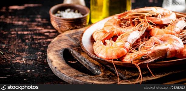 Boiled shrimp in a plate on a cutting board with spices. On a rustic dark background. High quality photo. Boiled shrimp in a plate on a cutting board with spices.