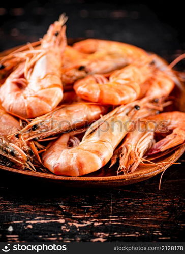 Boiled shrimp in a wooden plate. Against a dark background. High quality photo. Boiled shrimp in a wooden plate.