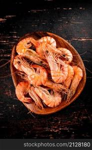 Boiled shrimp in a wooden plate. Against a dark background. High quality photo. Boiled shrimp in a wooden plate.