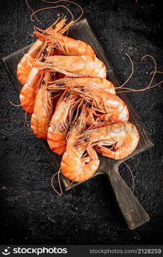 Boiled shrimp on a cutting board. On a black background. High quality photo. Boiled shrimp on a cutting board.