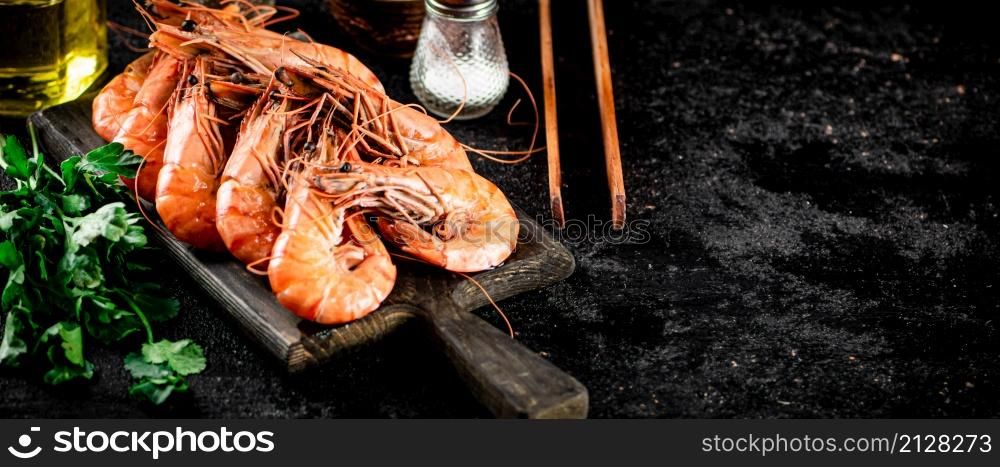 Boiled shrimp on a cutting board with parsley and spices. On a black background. High quality photo. Boiled shrimp on a cutting board with parsley and spices.