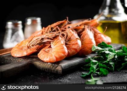 Boiled shrimp on a cutting board with parsley and spices. On a black background. High quality photo. Boiled shrimp on a cutting board with parsley and spices.