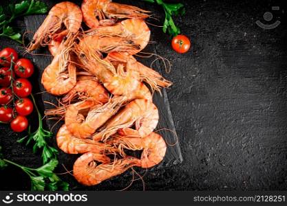Boiled shrimp on a stone board with tomatoes and parsley. On a black background. High quality photo. Boiled shrimp on a stone board with tomatoes and parsley.