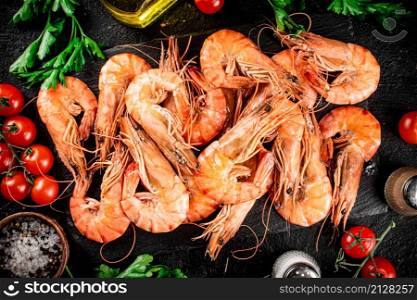 Boiled shrimp on a stone board with tomatoes and parsley. On a black background. High quality photo. Boiled shrimp on a stone board with tomatoes and parsley.