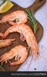 boiled shrimp prawns cooked in the seafood restaurant, fresh shrimps wooden cutting board plate with ice herbs and spices lemon rosemary