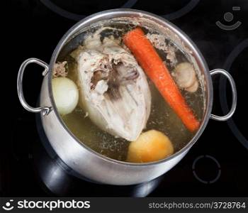 boiling of chicken broth with seasoning vegetables in steel pan on glass ceramic cooker