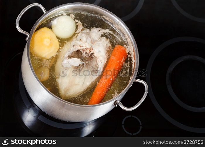 boiling of chicken soup with seasoning vegetables in steel pan on glass ceramic cooker