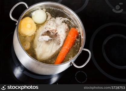 boiling of chicken soup with seasoning vegetables in steel pan on glass ceramic cooker