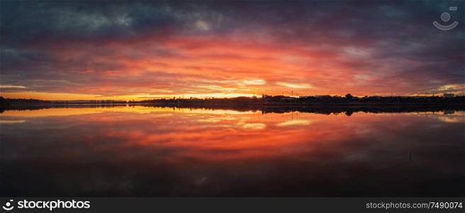 Bold sunset panorama over Delia lake, Moldova. Cloudy dusk sky and red sunlight reflection on the water surface. Dramatic dusk waterscape.