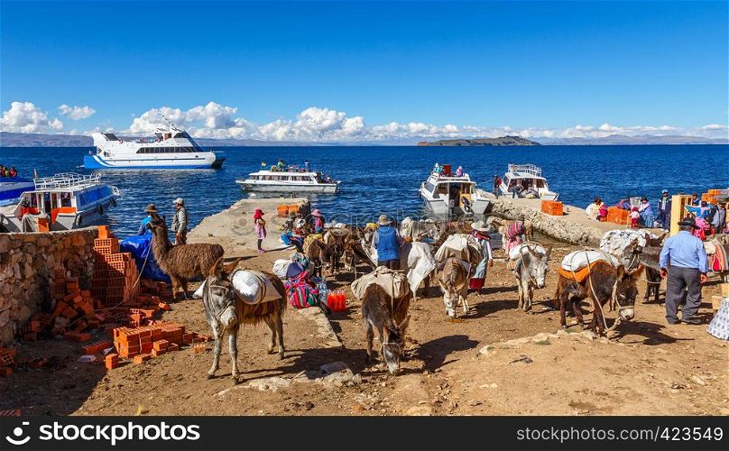 Bolivian peasants arrived by the ferry boat, gathered on the shore of Titicaca lake with heavy loaded donkeys in the foreground, Strait of Tiquina, Bolivia, South America