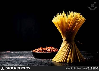 Bolognese sauce in a frying pan with a bunch of pasta dry. Against a dark background. High quality photo. Bolognese sauce in a frying pan with a bunch of pasta dry.