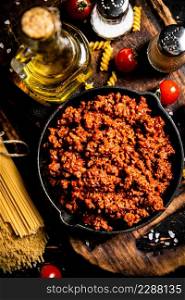 Bolognese sauce on a cutting board with cherry tomatoes and dry pasta. Against a dark background. High quality photo. Bolognese sauce on a cutting board with cherry tomatoes and dry pasta.