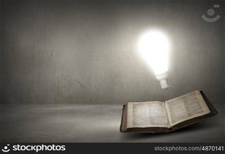 Book and light bulb. Old opened book and glowing light bulb